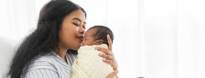 A woman gently cuddles a newborn in a yellow blanket, sitting together in a brightly lit room for medbridge patient care.