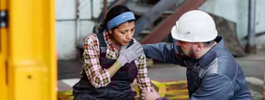 A construction worker holds her shoulder in pain as a colleague in a white hard hat kneels beside her, referencing medbridge.