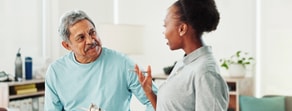 An older man listens as a woman, possibly a healthcare worker, discusses medbridge healthcare education in a bright room.