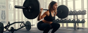 A woman in athletic wear squats with a barbell on her shoulders in a gym, showing fitness and medbridge healthcare training.