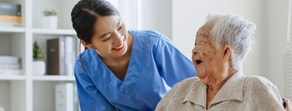 A nurse in blue scrubs smiles at an elderly woman in a wheelchair, illustrating medbridge's compassionate care.