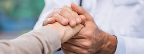 A person in a white coat gently holds another’s hand, symbolizing support in a medbridge healthcare training setting.