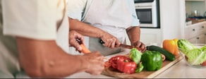 Two people in aprons slice vegetables together in a modern kitchen, showing teamwork like medbridge healthcare training.
