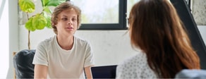 Two people sit indoors talking about healthcare training, with one wearing a white shirt and discussing medbridge.