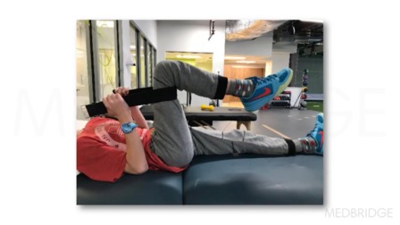 A person stretches with a strap on a therapy table, using hybrid care techniques at a gym, in collaboration with medbridge.
