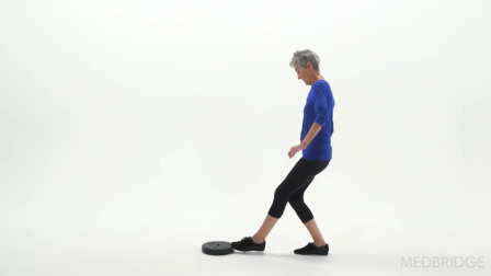 A person with short gray hair in a blue shirt balances on one leg, using Medbridge's healthcare training program.