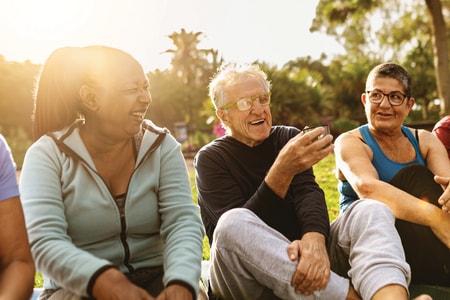 Older adults talk and smile on yoga mats in a sunny park, enjoying wellness activities with medbridge care software support.