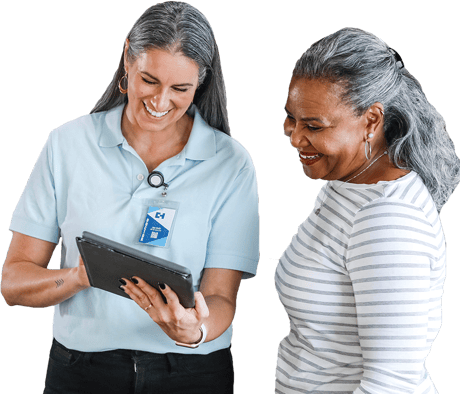 Two women smiling at a tablet, wearing a Medbridge polo and a striped shirt.
