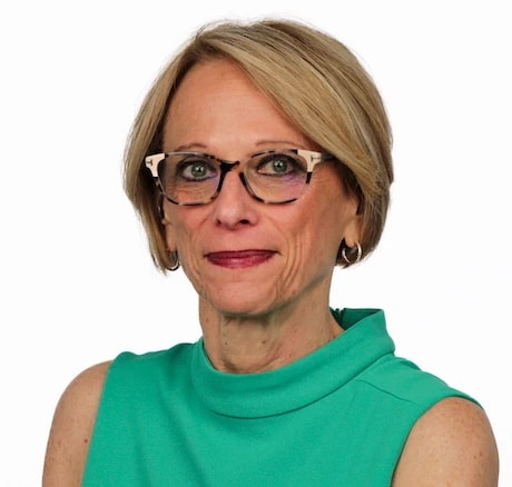 A woman with short blonde hair and glasses poses in a green top, representing confident medbridge digital healthcare professionals.
