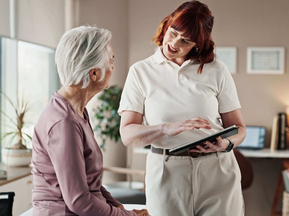 Clinician reviewing remote therapeutic monitoring (RTM) billing update with older patient using tablet in outpatient setting