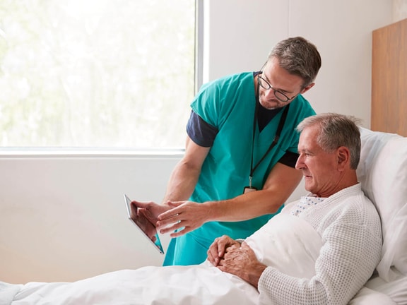 Clinician showing tablet to hospital patient during bedside assessment for disorders of consciousness rehabilitation.