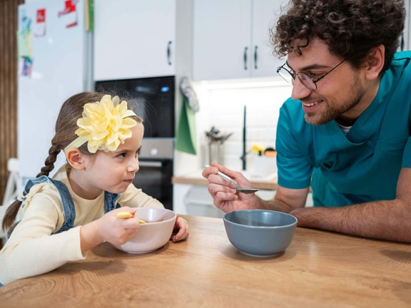 Feeding therapist supporting pediatric tube weaning readiness during a guided mealtime with a young child