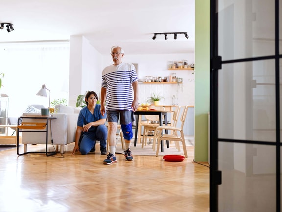 Physical therapist supporting intentional neuro rehab mobility training during balance and gait exercises at home.