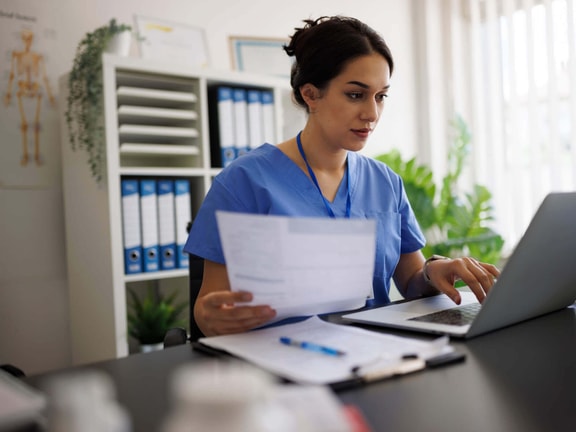 Outpatient clinician reviewing remote therapeutic monitoring (RTM) denied claims and billing documents on laptop in clinic office