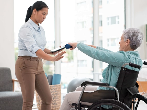 Physical therapist supporting seated balance and posture in an older adult with mobility limitations during rehabilitation care.