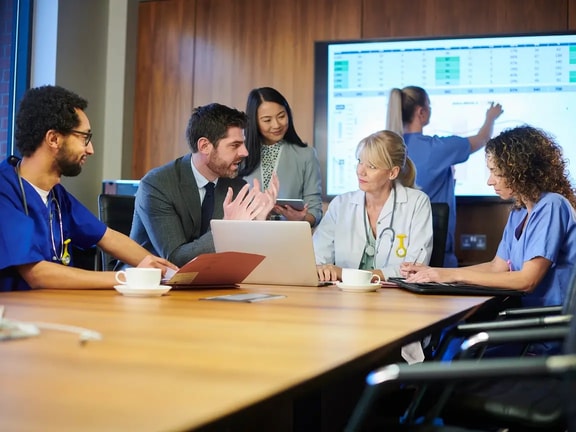 Healthcare team and analyst reviewing data dashboards in a meeting, discussing value-based care analytics strategies.
