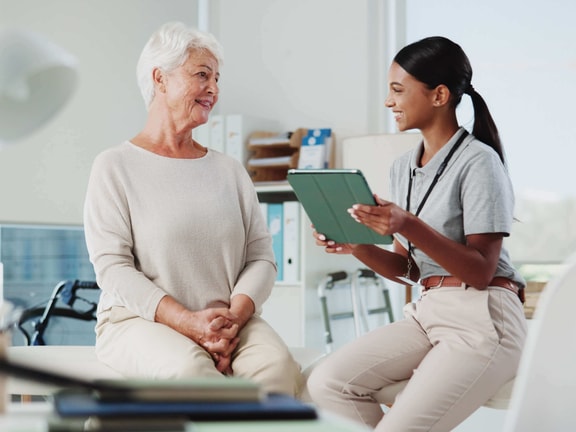 Clinician using tablet to discuss remote therapeutic monitoring with an older patient during a clinic visit.