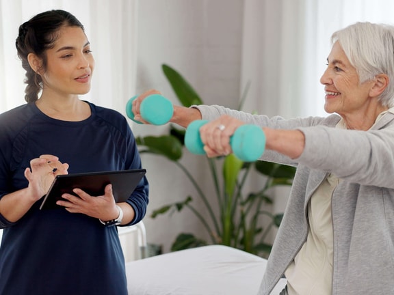 Physical therapist guides older patient using dumbbells during exercise, demonstrating technology-supported physical therapy care