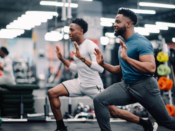Athletes performing lunges during return-to-sport strength training session in a gym.