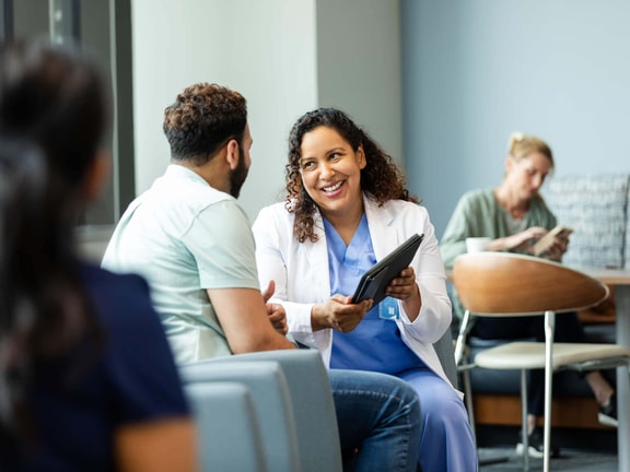 Clinician discussing care progress with a patient using a tablet to support patient-reported outcomes and remote therapeutic monitoring.