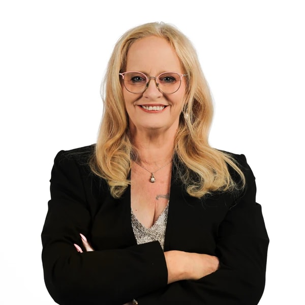 A blonde woman in glasses and a black blazer stands smiling with crossed arms, representing professionalism at medbridge.