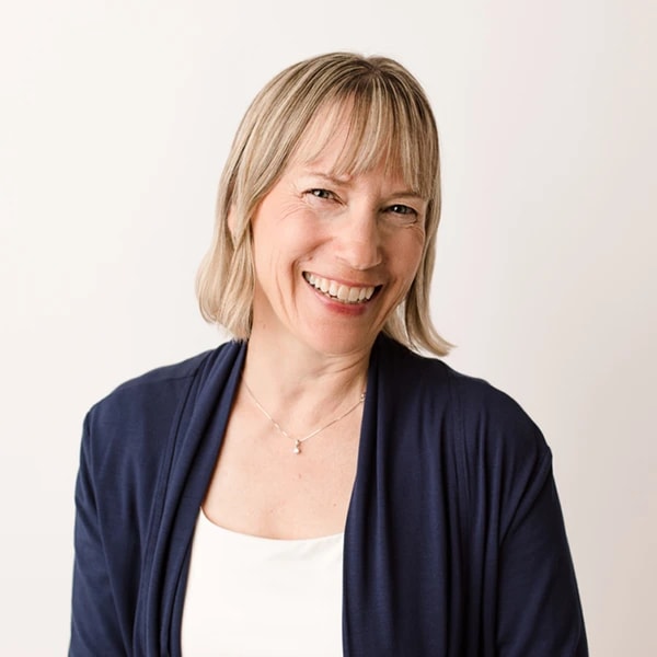 A smiling woman with light hair and bangs wears a navy cardigan over a white top on a white background for medbridge healthcare education.