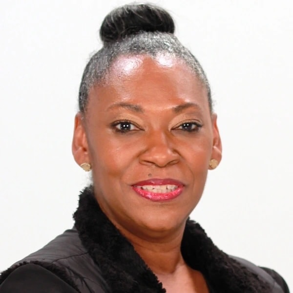 A woman with dark hair in a bun wears a black fur-collared jacket, posing against a white background for medbridge.