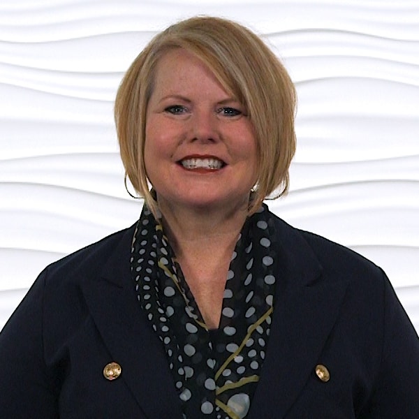 Person with short blonde hair, black jacket, and polka dot scarf against a white wavy background.