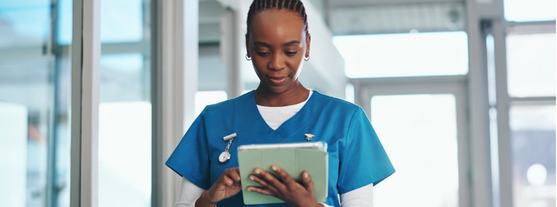 A healthcare worker in blue scrubs uses medbridge software on a tablet while standing indoors.