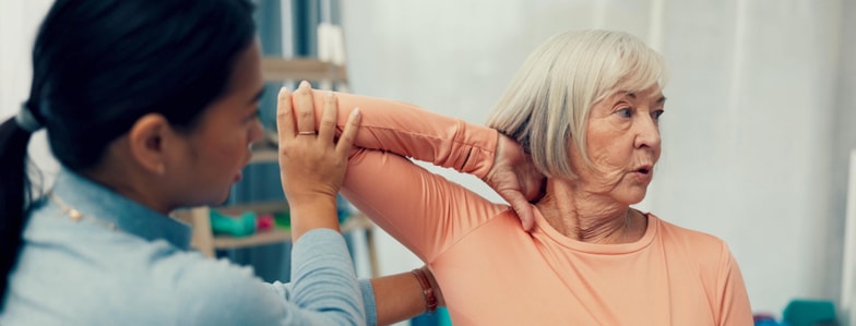 A woman helps an older woman stretch her arm during physical therapy, illustrating medbridge’s digital healthcare approach.