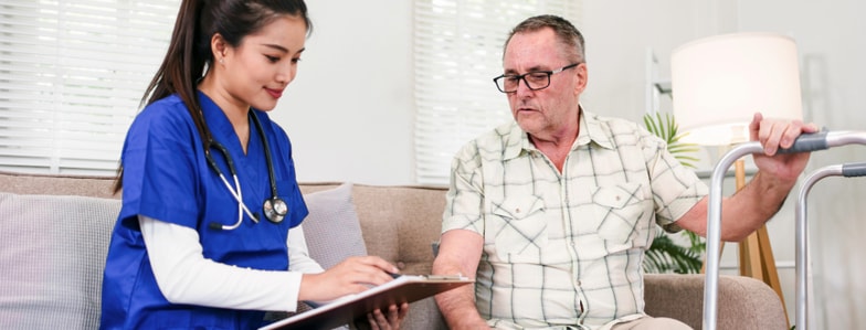 A nurse in blue scrubs discusses digital healthcare with an older man with a walker on a couch, referencing medbridge.