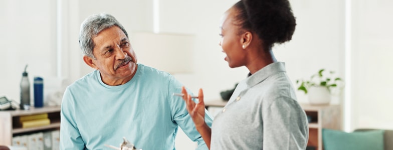An older man listens as a woman, possibly a healthcare worker, discusses medbridge healthcare education in a bright room.