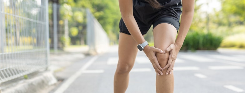 Person in athletic wear outdoors holding their knee, possibly in pain, representing medbridge healthcare education awareness.