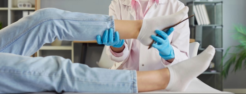 A healthcare professional in blue gloves checks a patient's ankle and foot on an exam table for medbridge training.