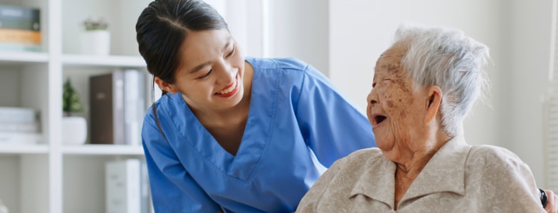 A nurse in blue scrubs smiles at an elderly woman in a wheelchair, illustrating medbridge's compassionate care.