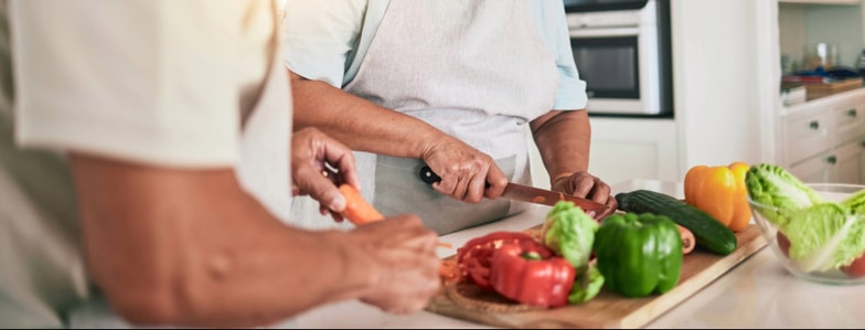 Two people in aprons slice vegetables together in a modern kitchen, showing teamwork like medbridge healthcare training.