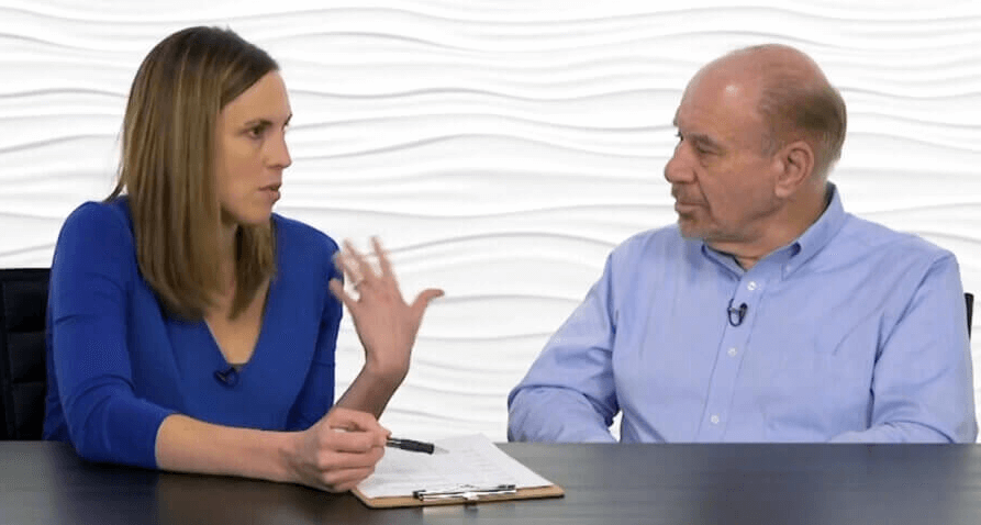 Two people discuss healthcare education at a table, focused on improving patient care software, with both in blue tops against a white background.