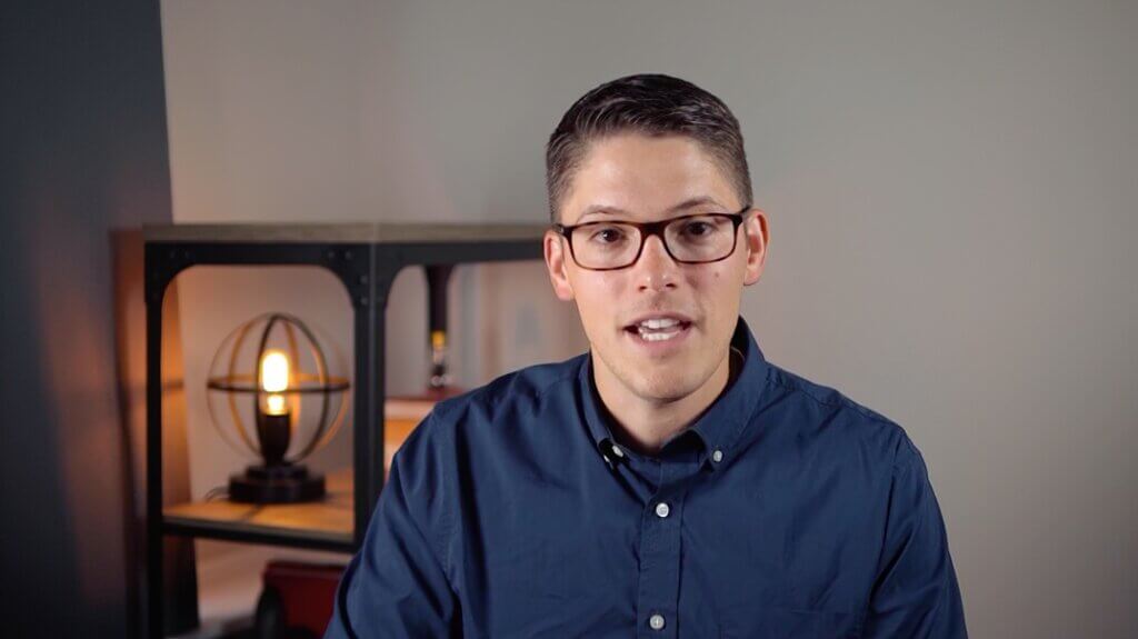 A person in glasses and a dark blue shirt discusses digital healthcare on camera with a warm lamp in the background.
