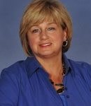 A person with short blonde hair smiles warmly in a blue shirt against a plain background, representing medbridge's digital healthcare.