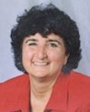 Individual with curly dark hair smiling in a red jacket, plain background.