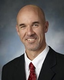 A bald man with a short beard, dressed in a suit and tie, smiles professionally representing medbridge innovations.