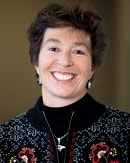 A person smiling in a patterned sweater and necklace radiates approachable elegance, embodying medbridge's healthcare education spirit.