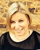 A smiling person with short blonde hair stands in front of a brick wall, highlighting their role in healthcare education at Medbridge.