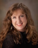 A curly-haired woman in a black top smiles warmly at the camera, embodying medbridge's compassionate healthcare education spirit.