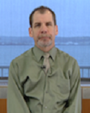 A person in a green shirt and tie sits by a window, reflecting on healthcare training and medbridge software.