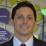 A smiling man in a suit and tie stands in front of a colorful digital healthcare-themed background, associated with Medbridge.