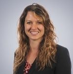 A young woman with curly hair in a dark blazer and patterned blouse smiles, embodying medbridge's commitment to digital healthcare.