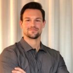 A confident person embodies the future of healthcare training with medbridge in a gray shirt against a light curtain backdrop.