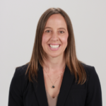 Woman with long brown hair in a black blazer on white background.