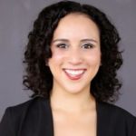 A smiling individual with curly black hair in a black blazer represents medbridge's healthcare education spirit.